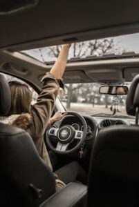 A young woman enjoying a drive with the sunroof open, showing car interior detail.