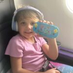Little girl with game and headphones on plane.