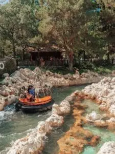 People enjoy a thrilling raft ride in a picturesque theme park setting surrounded by rocky terrain.