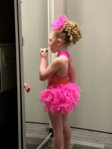 Child putting on lipstick before dance competition.