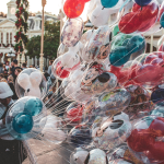 Colorful Mickey and Minnie balloons at a bustling theme park street.