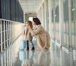 Side view full body of astonished cute little girl with kids suitcase and smiling mother pointing out window while walking together in contemporary airport hallway