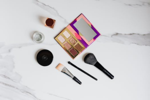 Flat lay of makeup essentials on a marble background, showcasing brushes and eyeshadow palette.