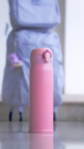 Close-up of a pink water bottle with a backpack in the background, ideal for travel and lifestyle themes.