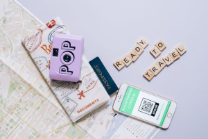 Travel essentials including a map, passport, camera, and smartphone with COVID-19 health passport for modern travel preparations.